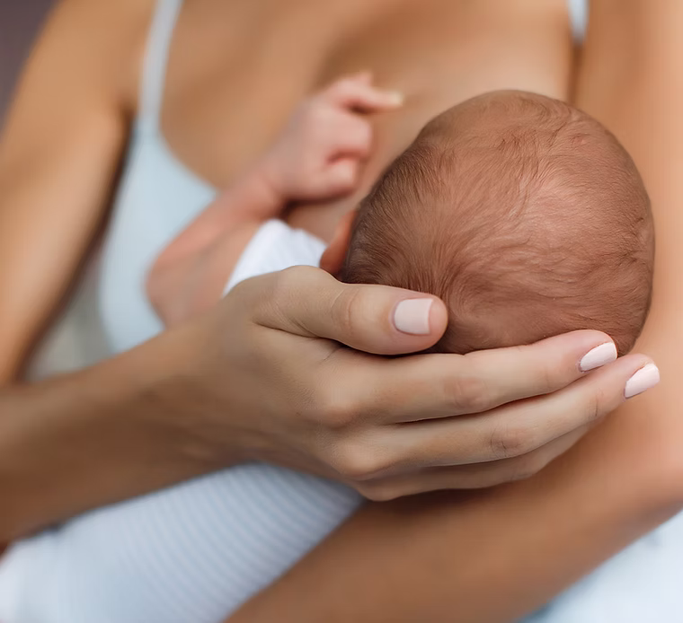 A new mother smiling while holding her baby, illustrating the benefits of our post-natal nutrition programs.